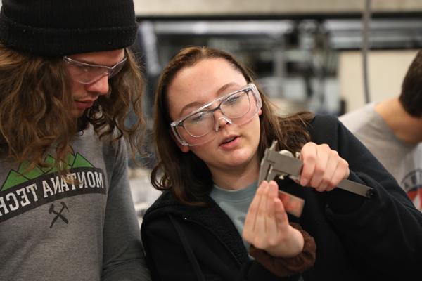 Two students measuring the thickness of a piece of metal